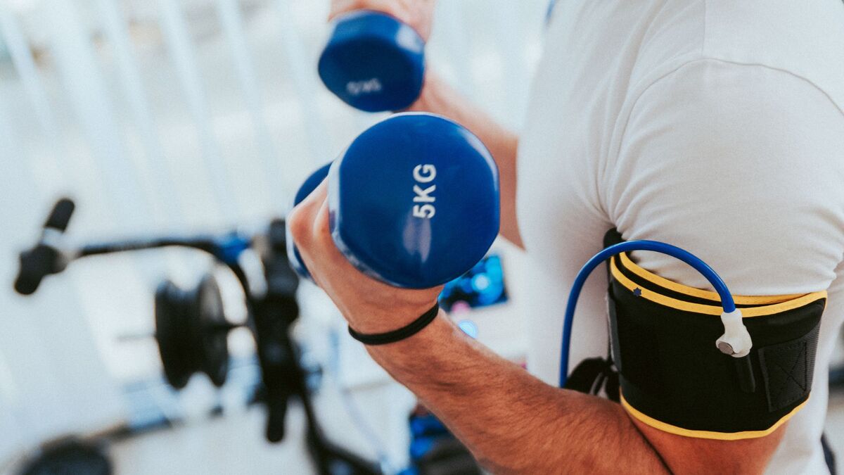 Person performing a dumbbell bicep curl with a blood flow restriction (BFR) band on their upper arm during occlusion training.